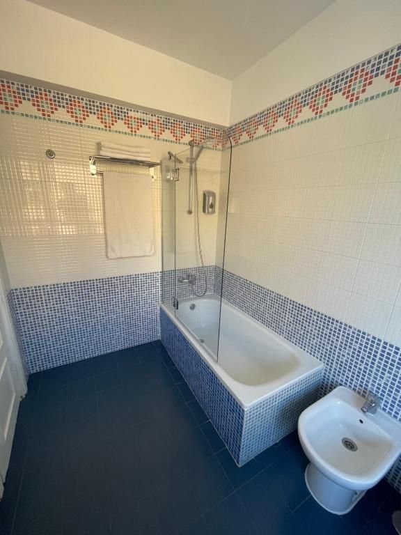 Cuarto de baño pequeño con azulejos, bañera, lavabo, toallero y suelo azul.