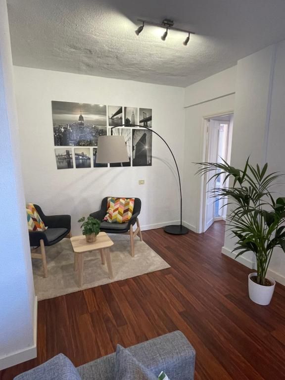Salón moderno con dos sillones estampados, una lámpara de pie, una mesa de centro, cuadros en la pared y una gran planta en maceta.