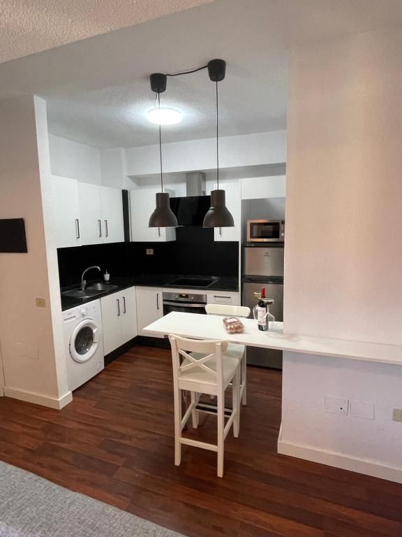 Cocina moderna blanca con suelo de madera oscura, salpicadero negro y una pequeña mesa de comedor con dos taburetes