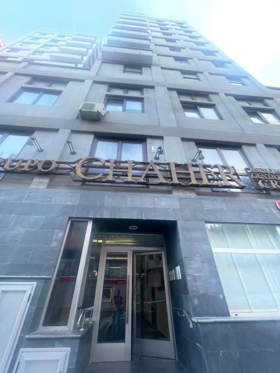 Edificio de apartamentos gris y alto, con una entrada de cristal y un letrero encima de la puerta