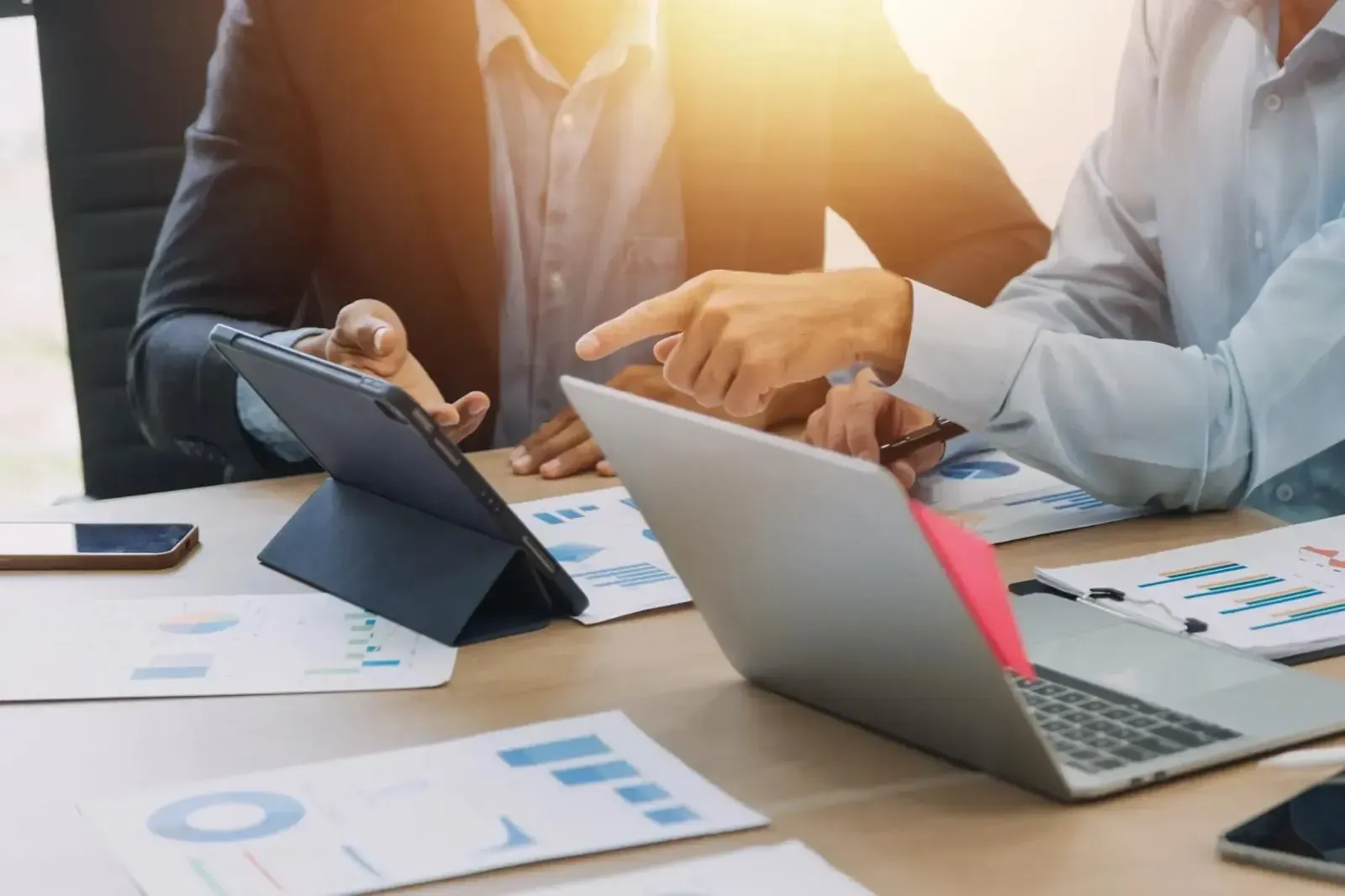 Reunión de negocios con manos apuntando a la tableta y la computadora portátil, gráficos sobre la mesa.