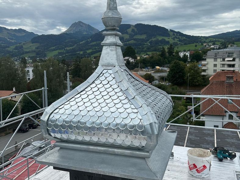 Gros plan d'un clocher en forme de dôme avec des écailles métalliques brillantes sur un toit, des montagnes en arrière-plan.