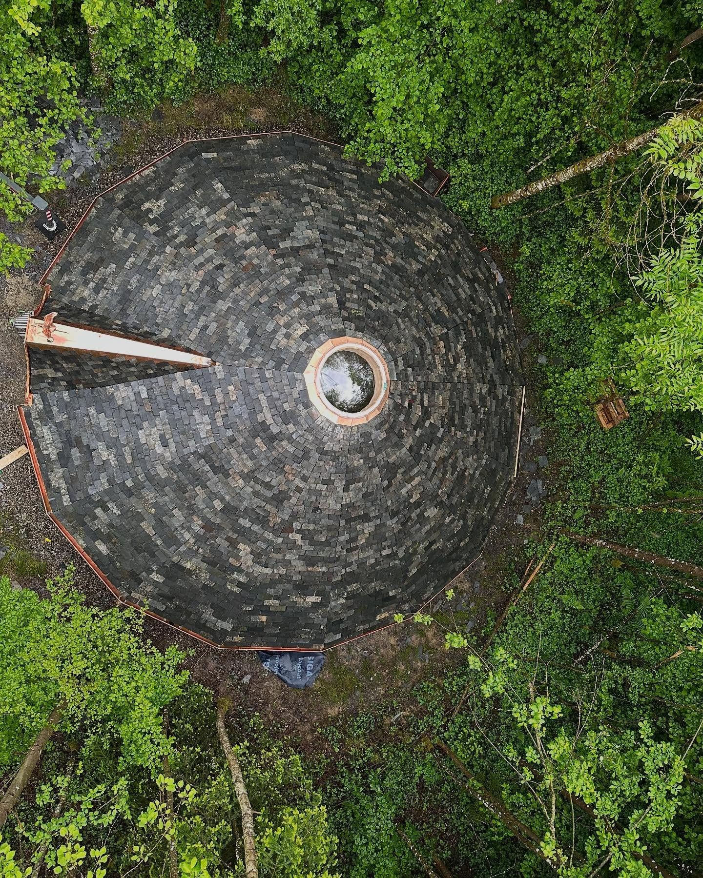 VuStructure en forme de dôme au toit sombre et texturé, entourée d'arbres verdoyants.