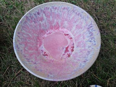 Un recipiente de color rosa y morado reposa sobre un exuberante campo verde.