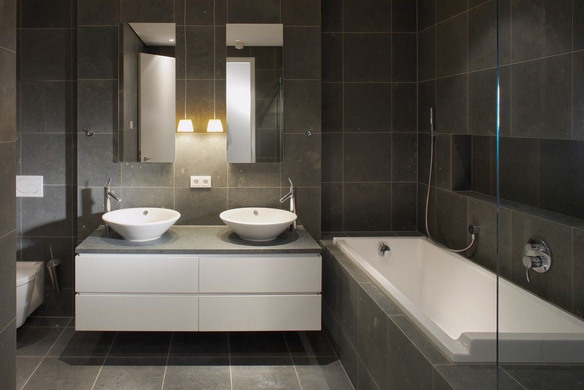 Salle de bains moderne avec double vasque, grand miroir et baignoire sur murs carrelés foncés