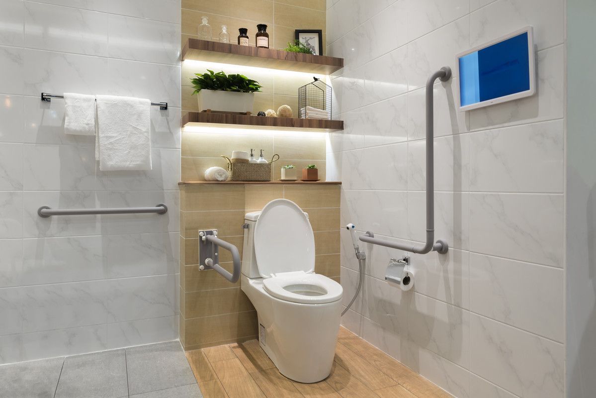 Salle de bain accessible avec toilettes, barres d'appui, étagères et écran mural