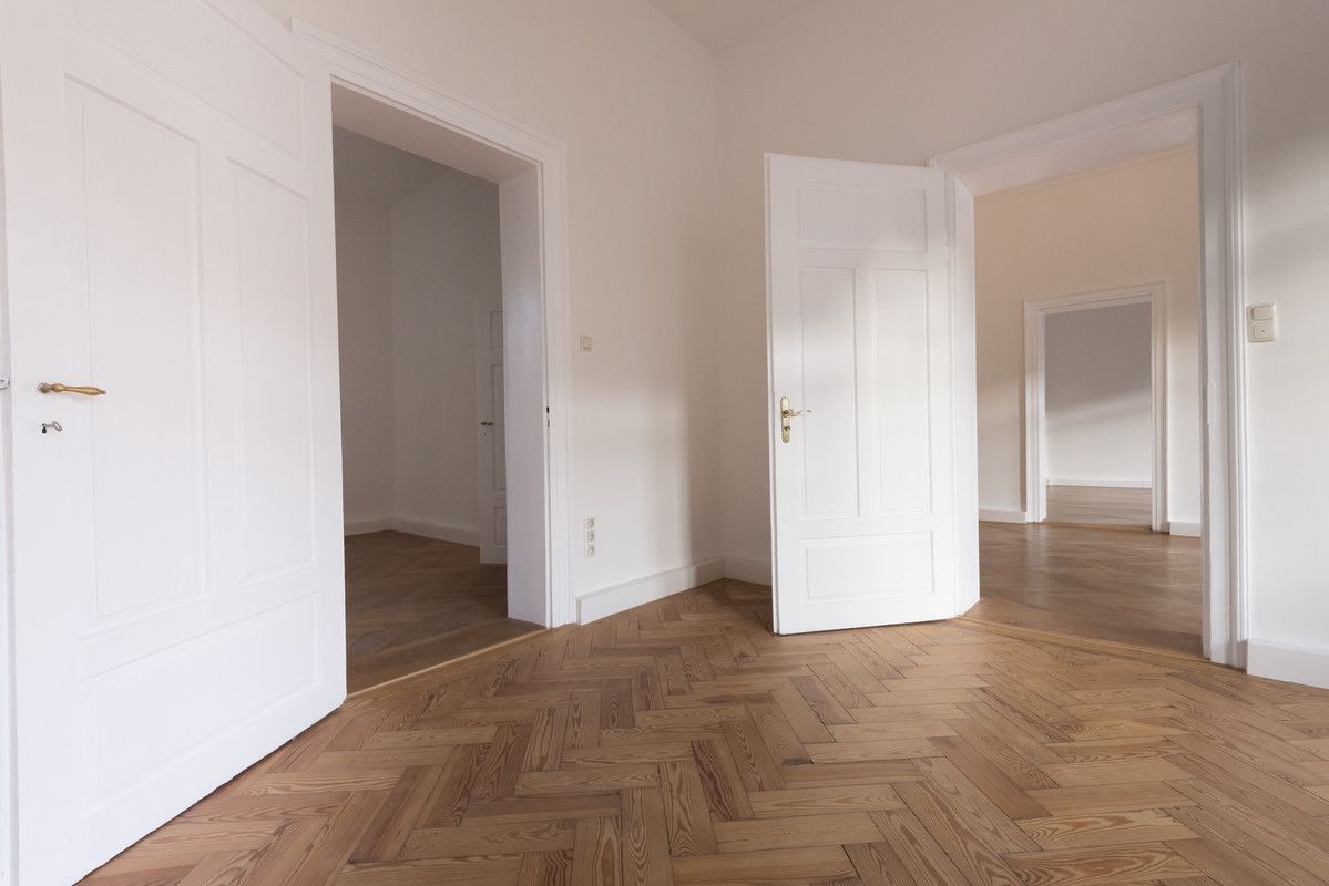 Pièce blanche vide avec parquet à chevrons et portes ouvertes donnant sur des pièces adjacentes