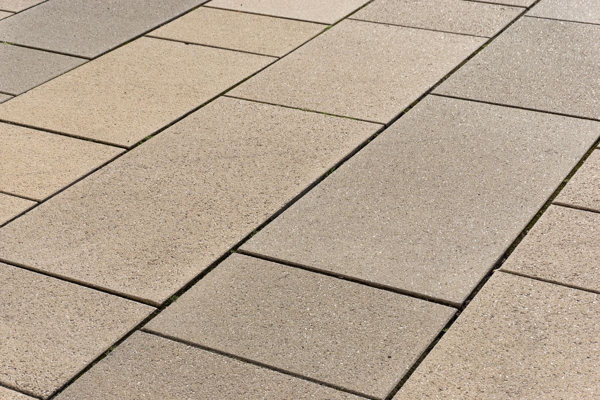 Gros plan sur des dalles de pavage en pierre beige et grise disposées selon un motif géométrique.