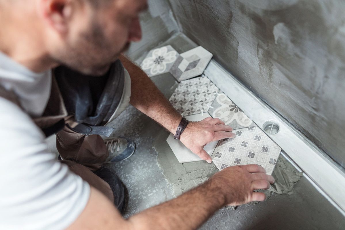 Une personne installe des carreaux de sol à motifs sur une surface en béton lors de la rénovation d'une maison