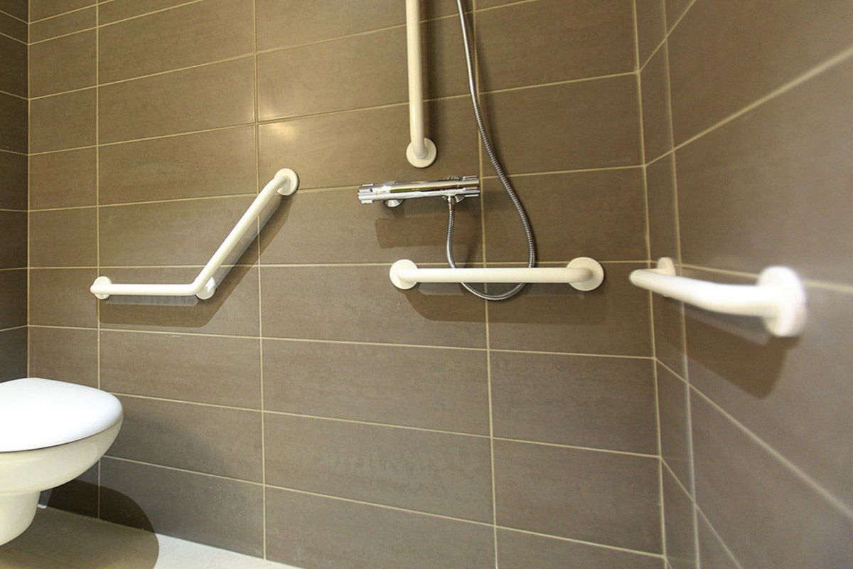 Salle de bain accessible avec barres d'appui murales et siège de douche à côté d'un lavabo