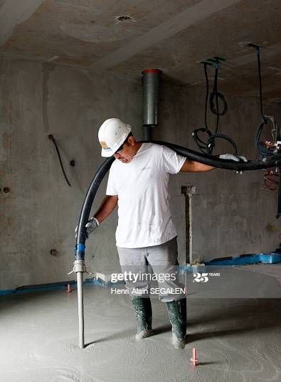 Ouvrier portant un casque de chantier utilisant un tuyau bleu dans une pièce en béton inachevée
