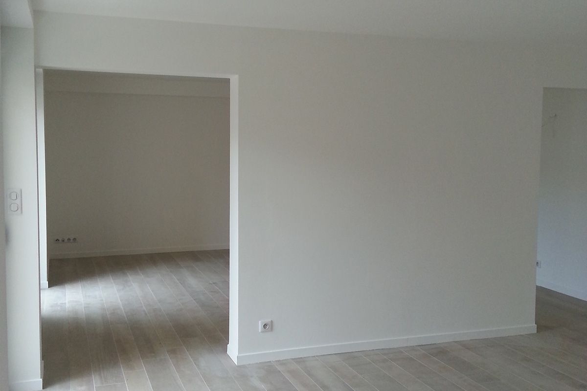 Chambre vide non meublée avec murs blancs, parquet clair et une large porte donnant sur une autre pièce