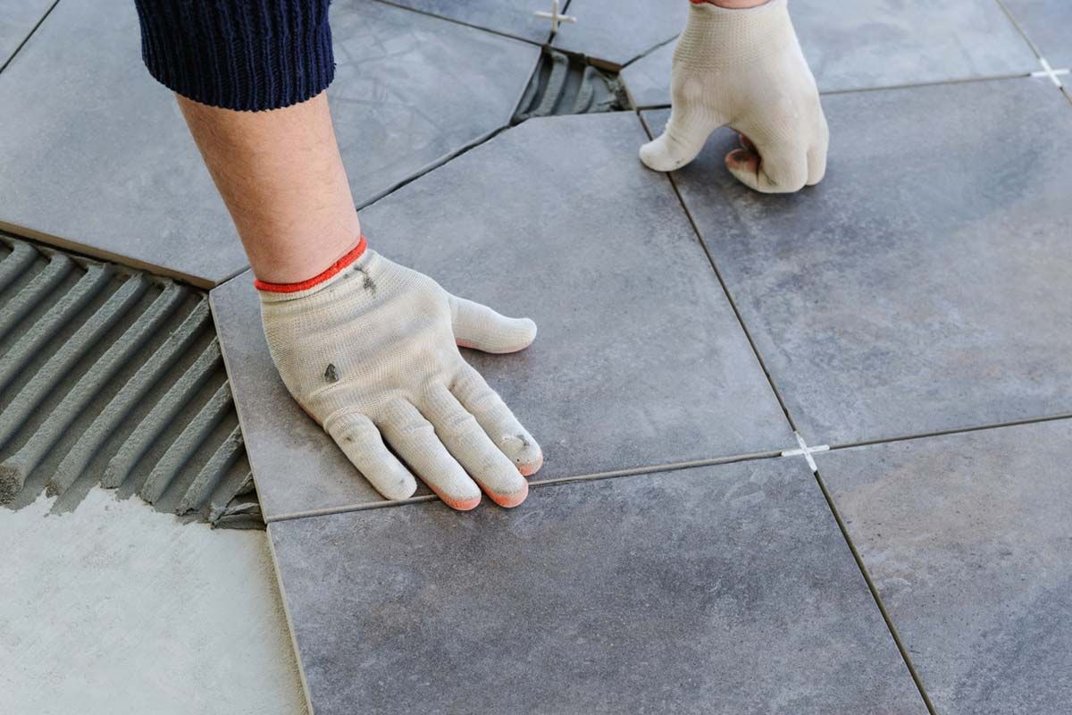 Des mains gantées alignent des dalles grises à côté d'une grille d'égout.