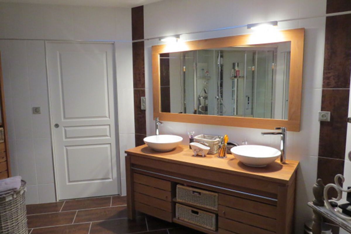 Salle de bains moderne avec double vasque, grand miroir, meuble-lavabo en bois et murs carrelés
