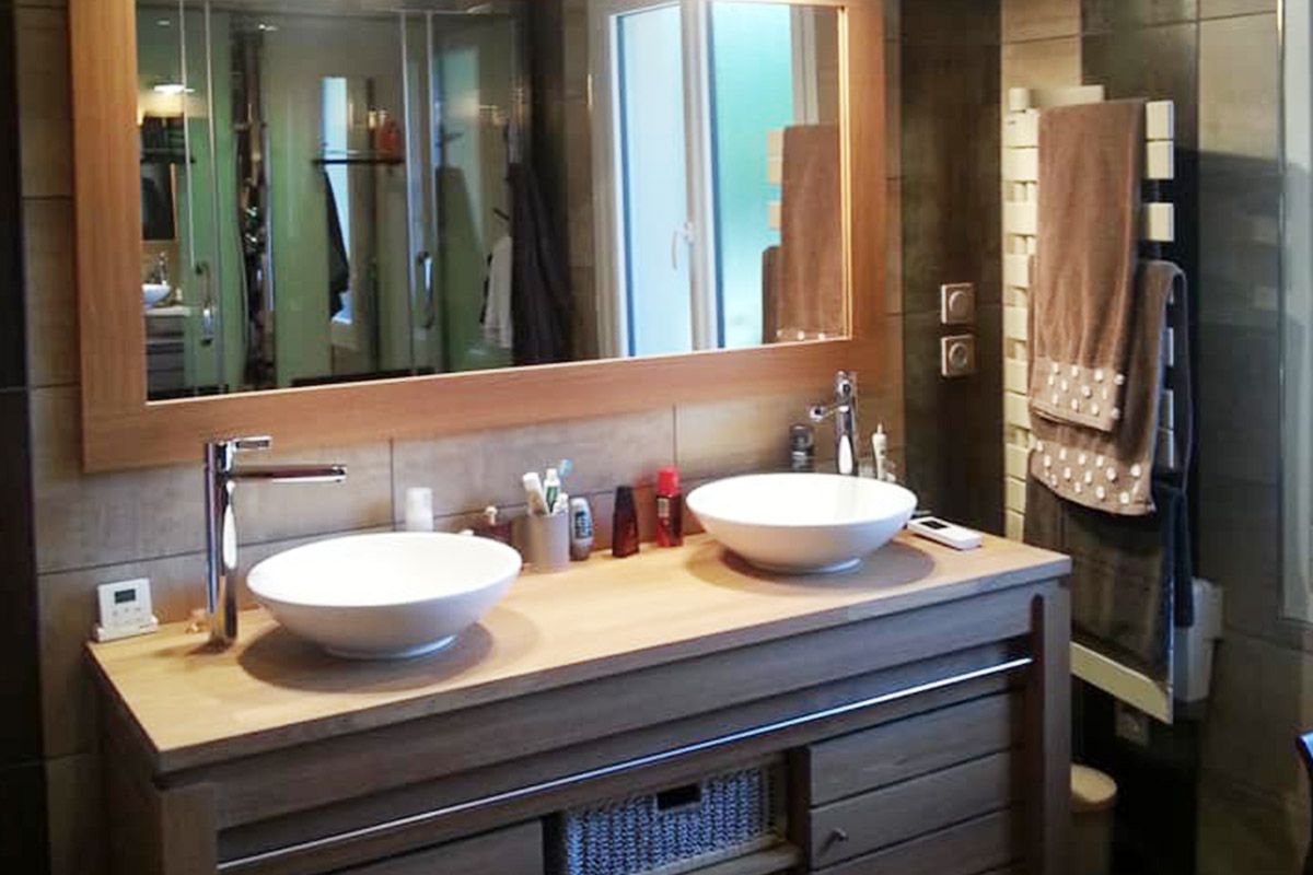 Meuble-lavabo moderne avec deux vasques blanches, un grand miroir et des armoires en bois beige.
