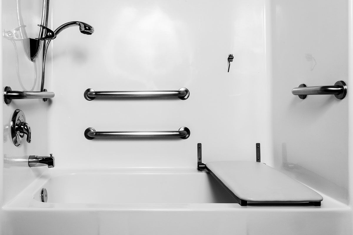 Baignoire blanche accessible avec barres d'appui, douchette et siège rabattable dans une salle de bains