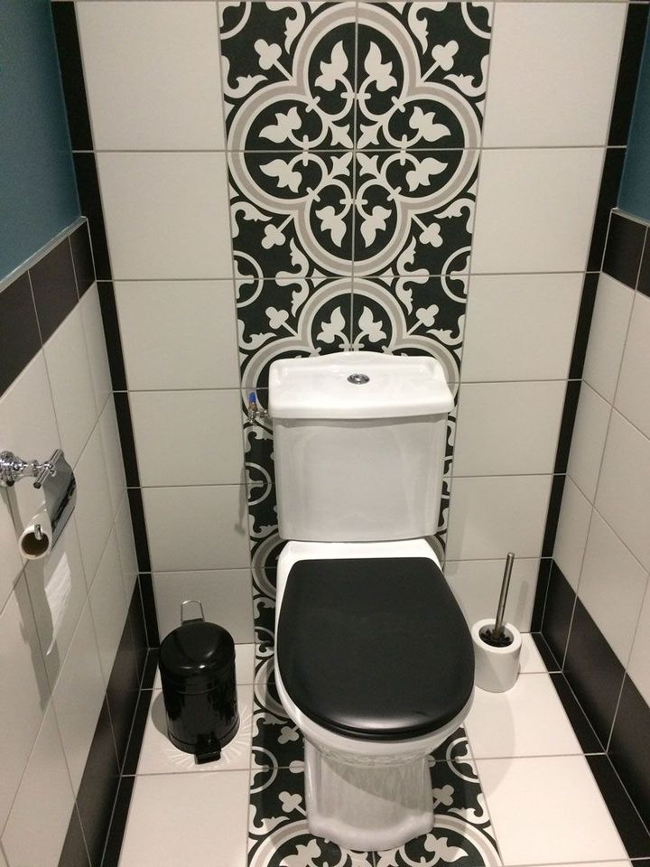 Petite salle de bains carrelée avec toilettes, panneau mural à motifs et porte-brosse de toilette.