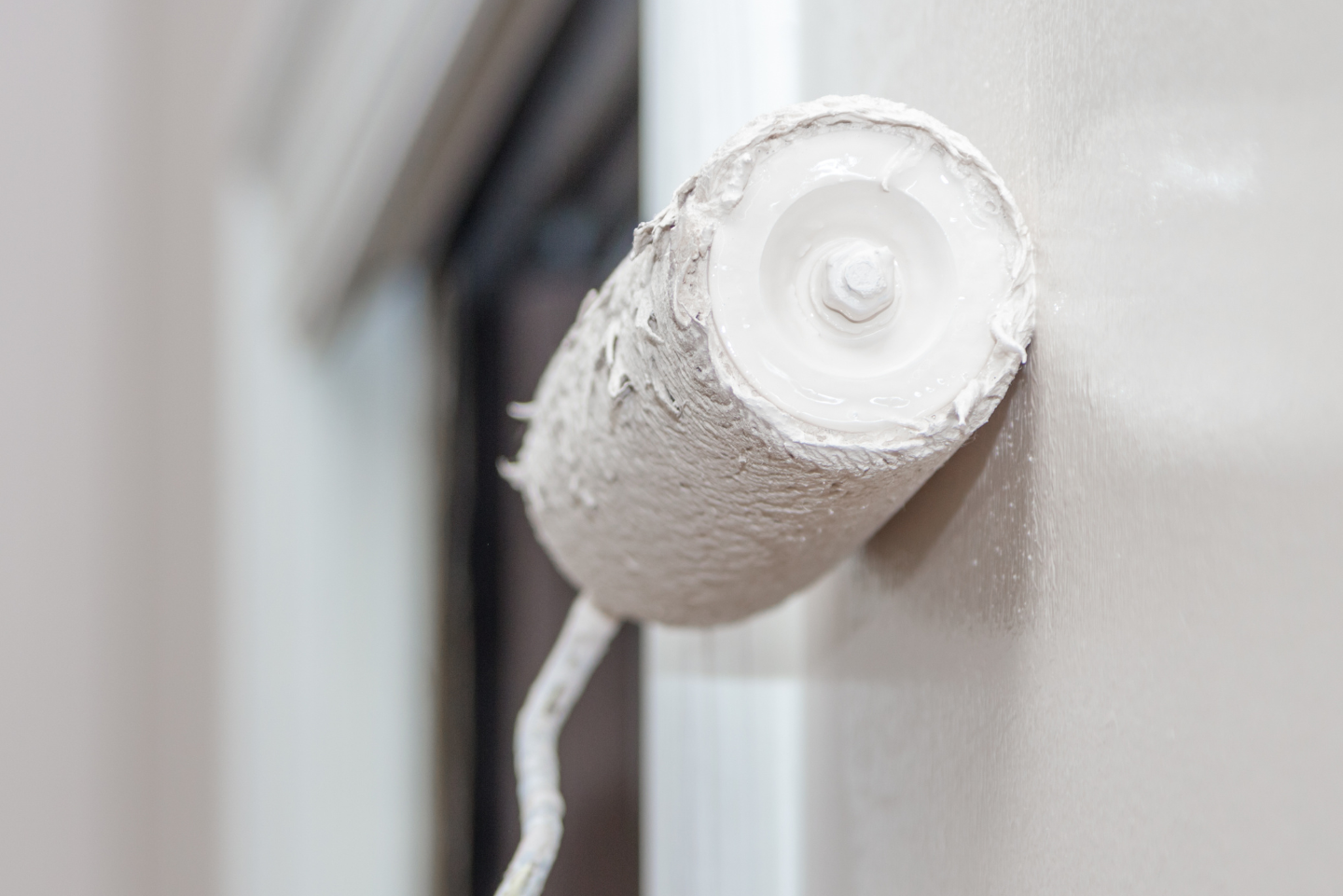 Rouleau à peinture recouvert de peinture blanche posé sur un mur blanc.