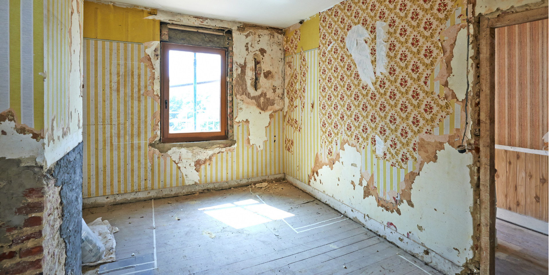 Intérieur de la chambre avec papier peint et fenêtre décollés ; chambre en cours de rénovation.
