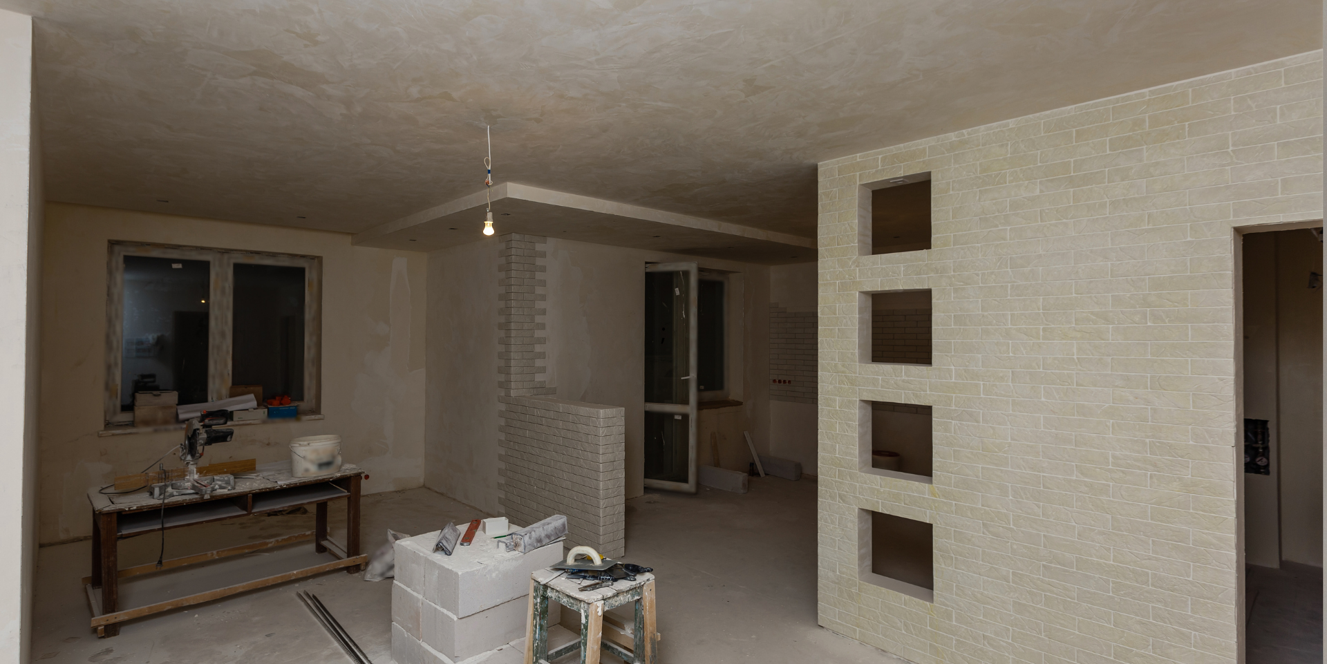 Intérieur d'une pièce en construction avec murs, fenêtres et matériaux de construction non finis.