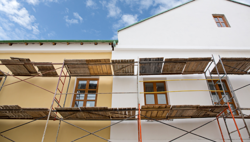 Bâtiment en cours de rénovation avec murs peints en jaune et blanc, échafaudages et fenêtres.