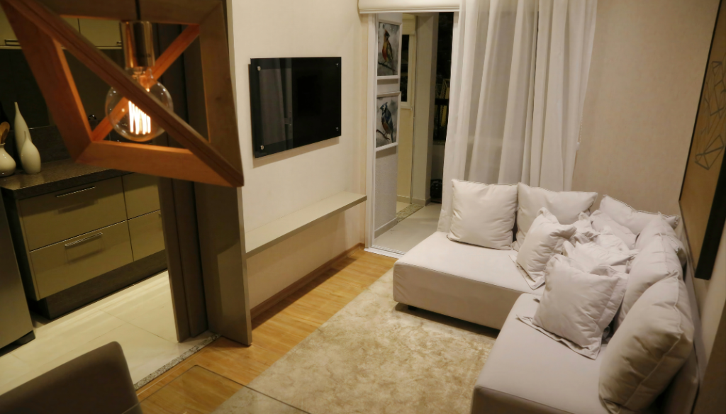 Séjour avec canapé sectionnel beige, TV, suspension et parquet en bois clair.