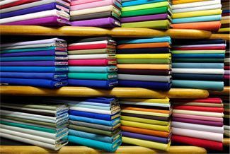 Pilas de rollos de tela de colores en estantes de madera.
