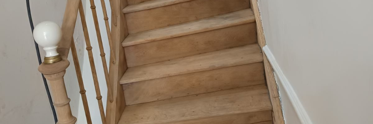 Escalier intérieur en bois clair avec marches, contremarches et rampe à barreaux tournés.
