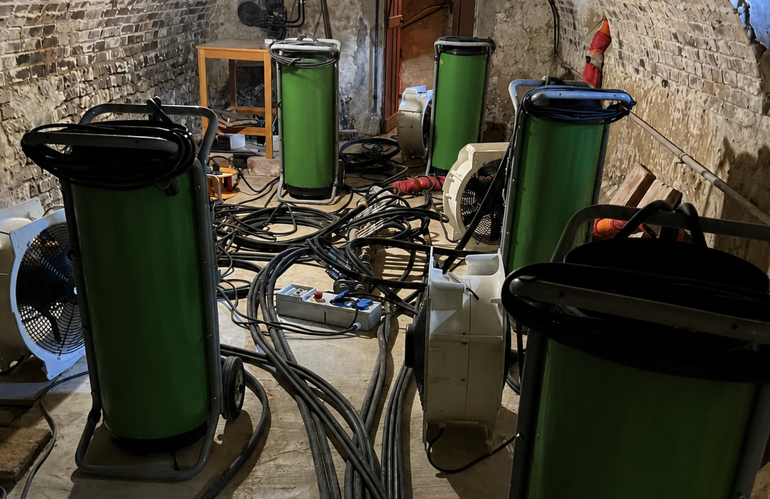 Pièce équipée de plusieurs appareils cylindriques verts reliés par des câbles et des ventilateurs, installés dans un espace intérieur aux murs en maçonnerie apparente.