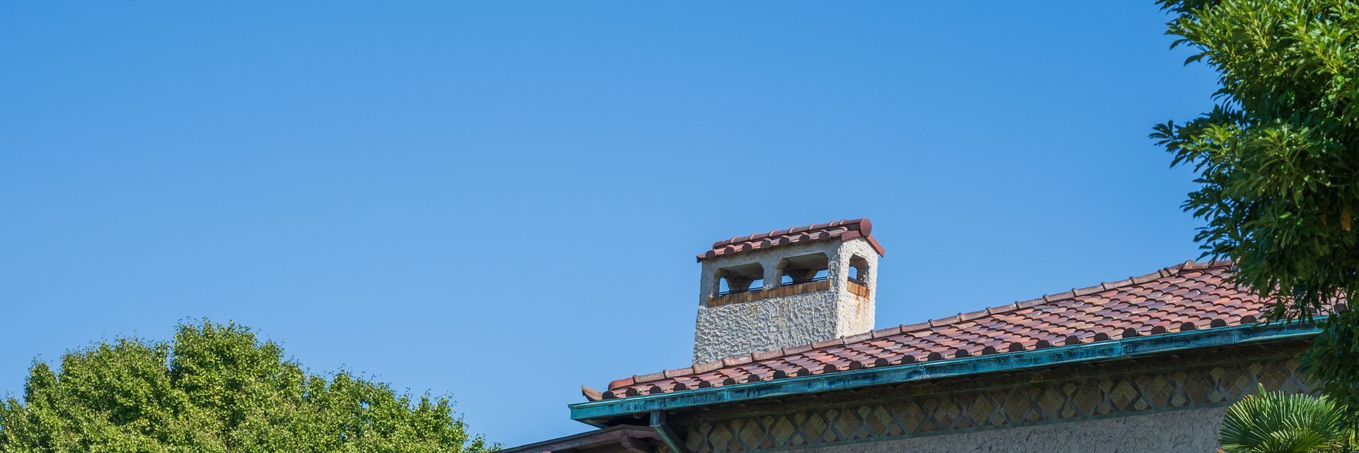 Toiture recouverte de tuiles rouges avec une cheminée maçonnée visible sur fond de ciel bleu.