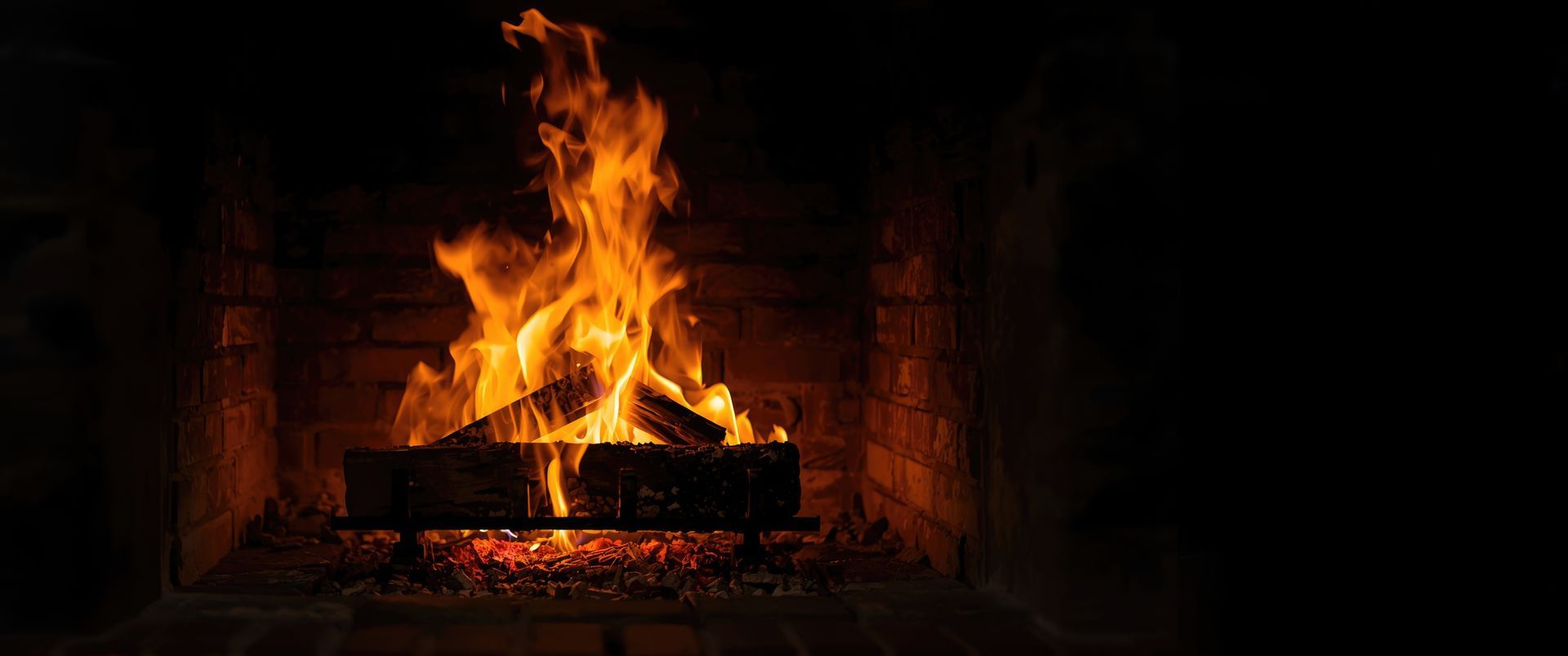 Bûches en bois en combustion dans un foyer de cheminée en briques, avec des flammes visibles au-dessus des braises.