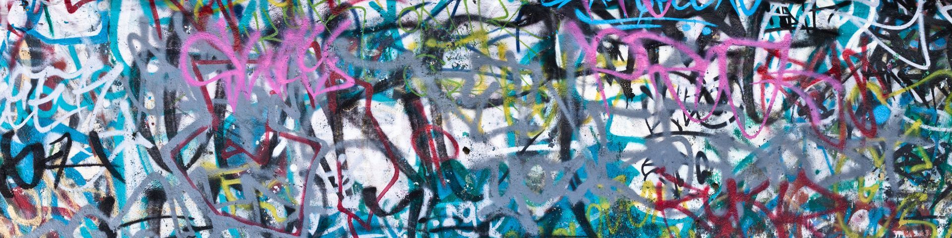 Mur recouvert de nombreux graffitis colorés superposés, composés de traits, formes et inscriptions peintes à la bombe.
