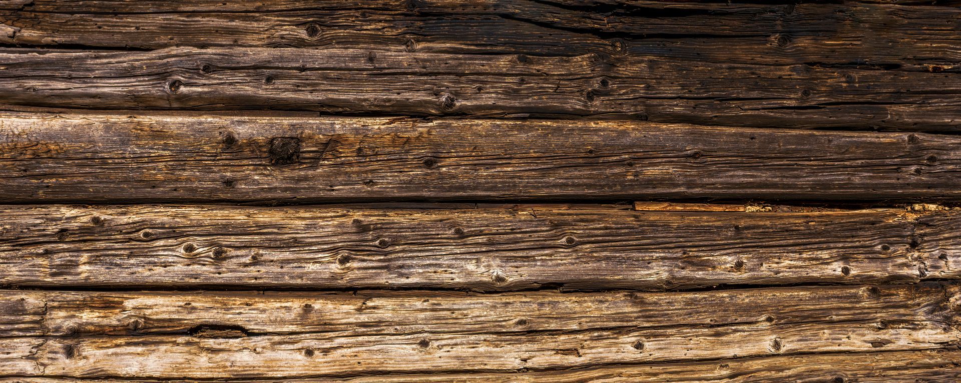 Surface composée de madriers en bois superposés avec des nœuds, fissures et variations de teinte.