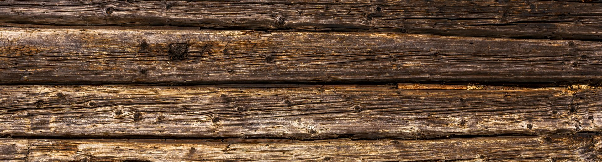 Planches en bois brun foncé présentant des fissures, des nœuds et un veinage prononcé.