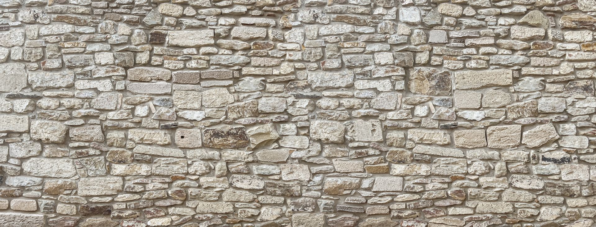 Mur en pierres apparentes composé de blocs de tailles et de formes variées assemblés avec des joints visibles.