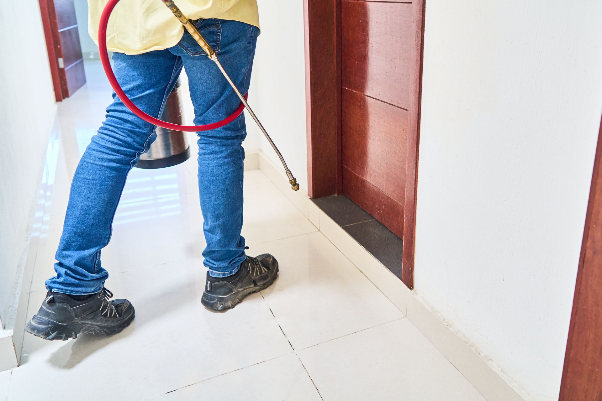 Personne tenant une lance de pulvérisation orientée vers le bas d'une porte dans un couloir intérieur carrelé.