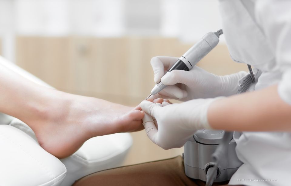 Pediküristin benutzt in einem Salon einen Nagelfräser am Fuß einer Kundin