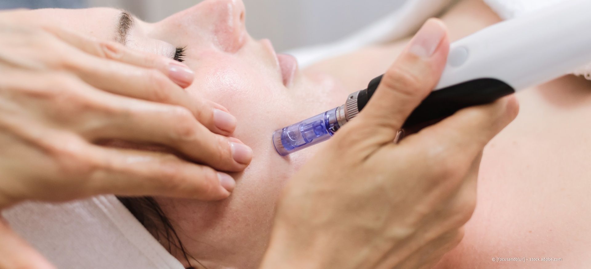 Hände, die mit einem violetten Pinsel eine Gesichtsbehandlung auf das Gesicht einer Person auftragen