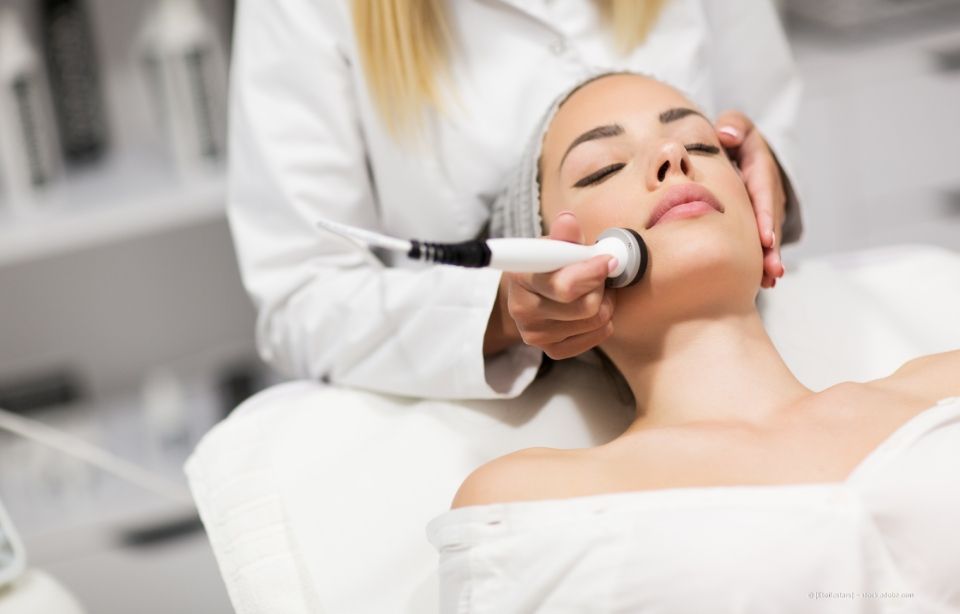 Frau erhält in einem Spa eine Gesichtsbehandlung mit einem handgeführten Hautpflegegerät