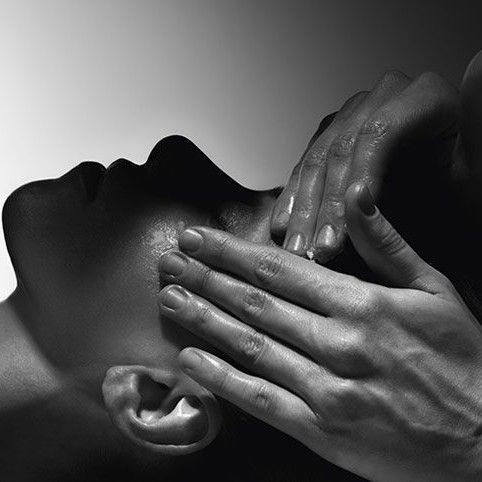 Primer plano en blanco y negro de un rostro al que unas manos tocan suavemente, sugiriendo cuidados o masaje.