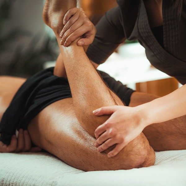 Masajista amasando la pierna de un cliente en una camilla de tratamiento en un entorno de spa.