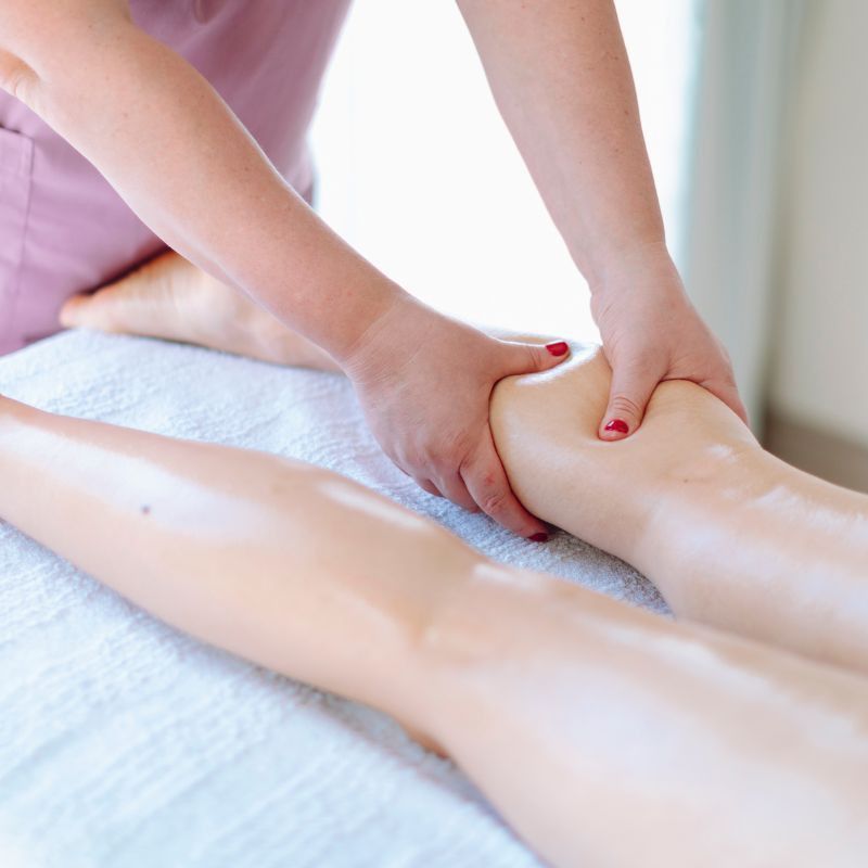 Manos masajeando las piernas de una persona con loción blanca en una camilla de spa.