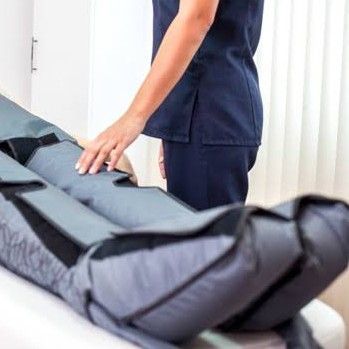 Una persona con uniforme quirúrgico azul marino revisa la pierna de un paciente en una mesa de tratamiento médico.