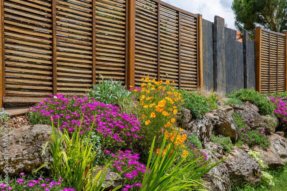 Des fleurs colorées fleurissent devant une clôture en bois et en pierre.
