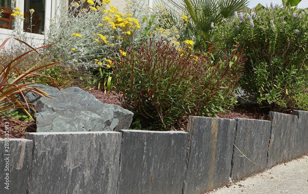 Mur de soutènement en pierre noire avec fleurs et feuillages colorés.