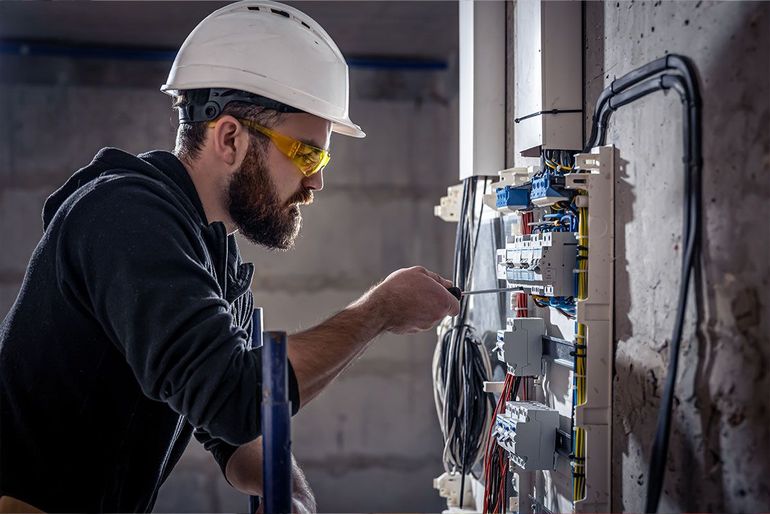 Ein Mann mit Schutzhelm und Schutzbrille arbeitet an einem Schaltkasten.