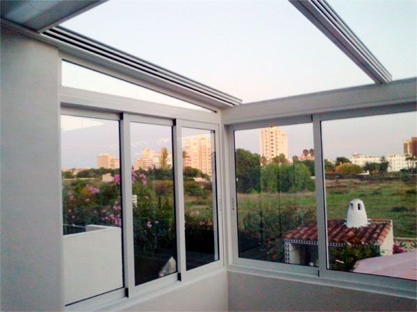 Terraza acristalada con puertas corredizas y techo retráctil, con vistas a la ciudad y al paisaje verde.