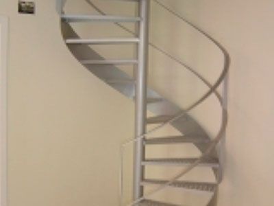 Escalera de caracol, construcción metálica, contra una pared beige.