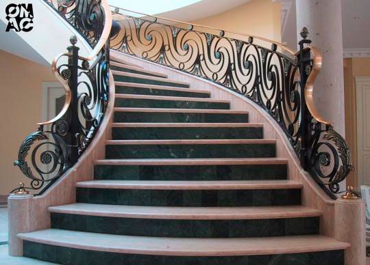 Escalera curva adornada con barandilla de metal negro y escalones de mármol verde.