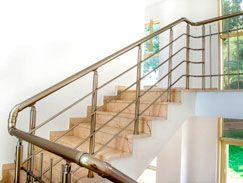 Escalera con pasamanos metálicos y peldaños de color claro sobre una pared blanca y una ventana.